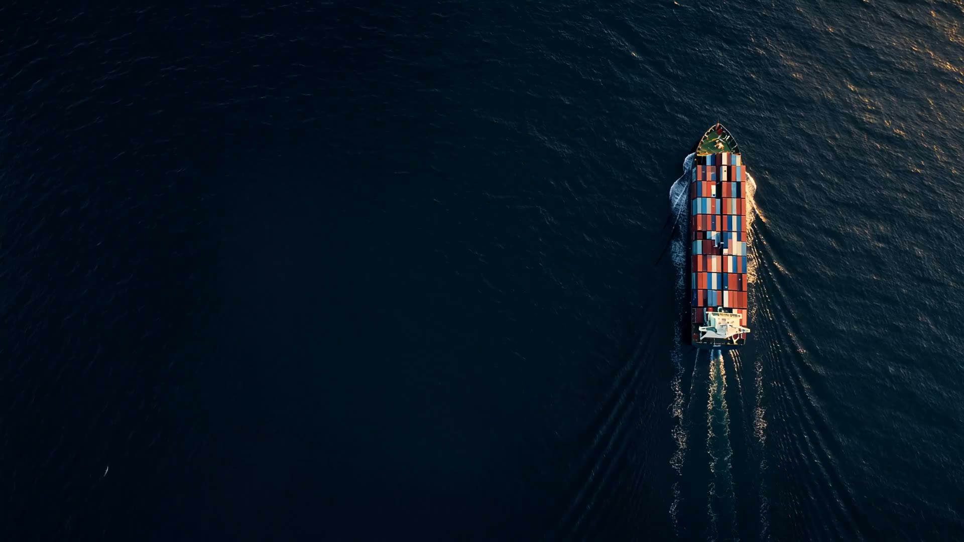A container ship under way on open ocean at low sun, seen from directly above.